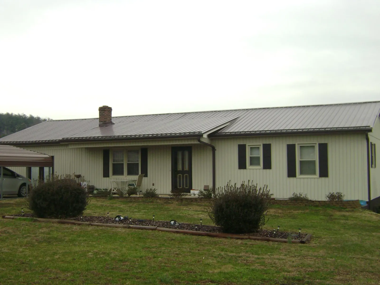 Brown metal roof on a cream sided ranch home with a brick chimney in Randolph